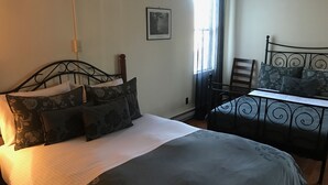 A bedroom with a bed, a chair, a table, and a window with curtains. - Dominion Hotel (Minden Hills)