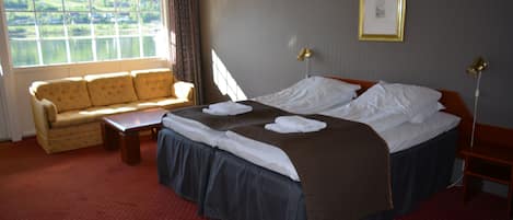 Une chambre d’hôtel avec un lit, un canapé, une table et une fenêtre donnant sur un lac.