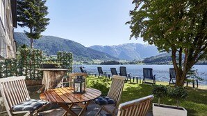 An outdoor seating area with a wooden table and chairs, a small tree, and a view of a lake with mountains in the background. - Strand Fjordhotel (Ulvik)