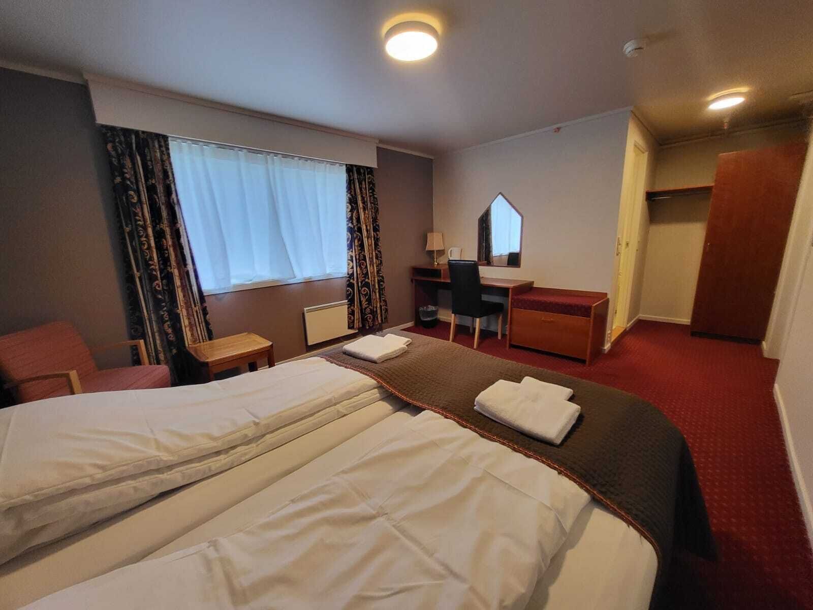Una habitación de hotel con una cama grande, un escritorio, una silla, un aparador y un espejo.