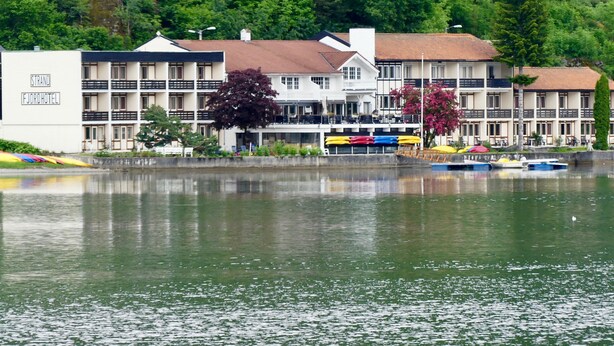 A waterfront hotel with multiple balconies, a swimming pool, and a row of colorful umbrellas. - Strand Fjordhotel (Ulvik)