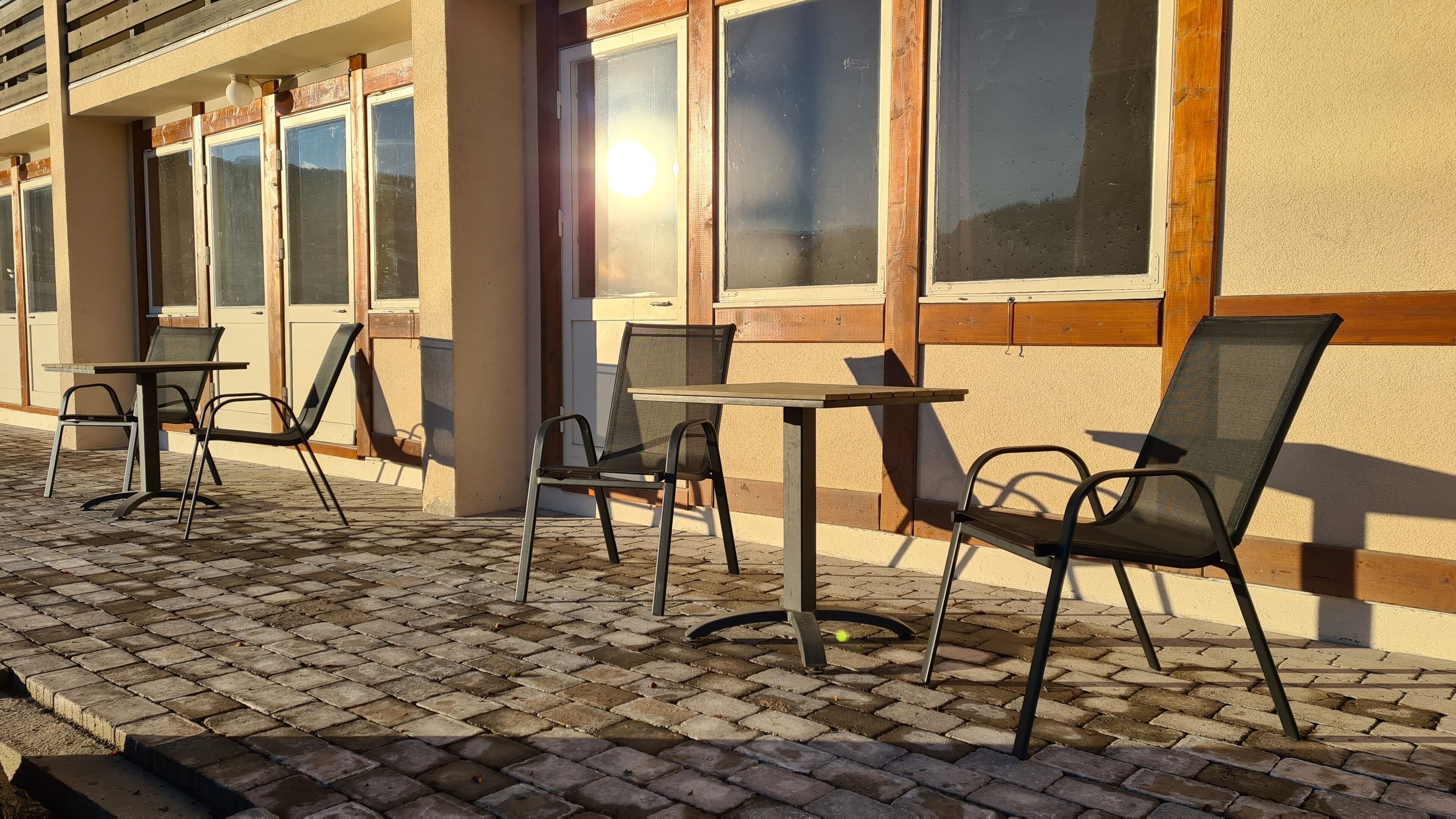 An outdoor seating area with tables and chairs, a brick pavement, and a building with large windows.
