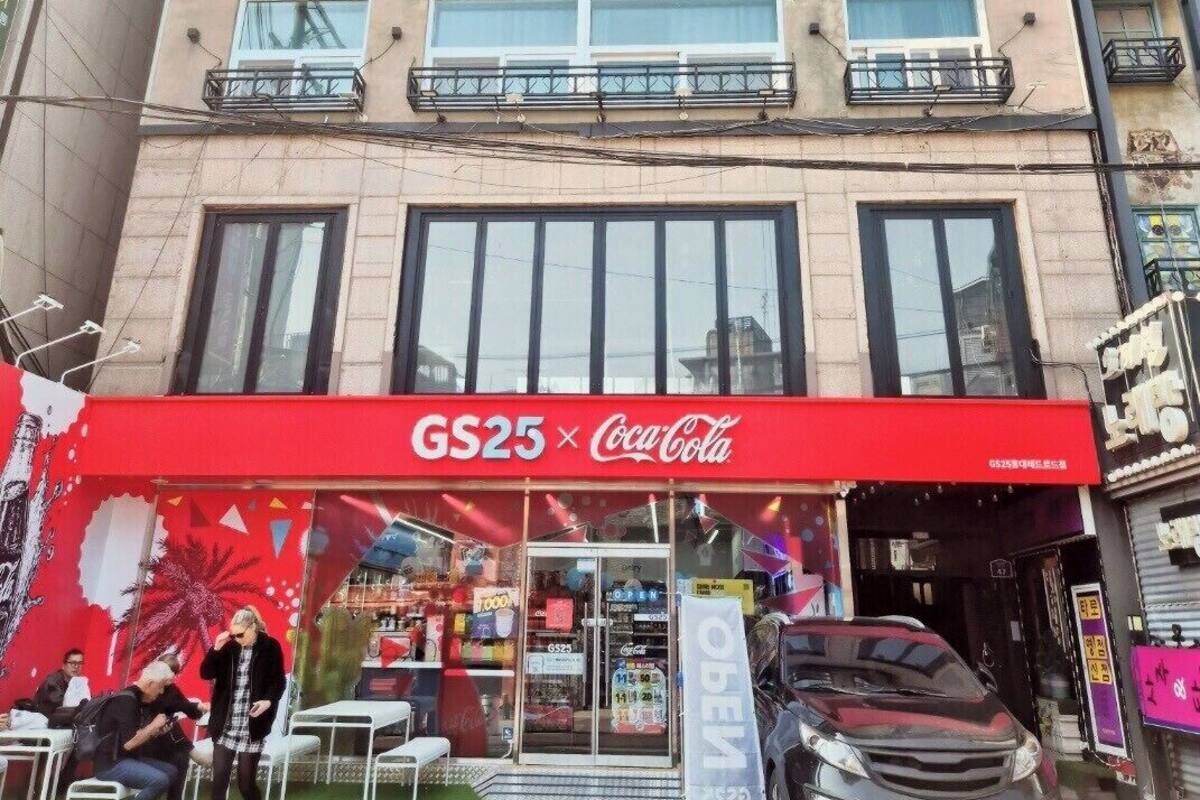A building with a red Coca-Cola sign, a car parked in front, and a sign for 'Guest House'.