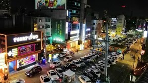 Una calle iluminada en la noche con un edificio brillante que muestra un letrero de neón para un bar o local de entretenimiento.