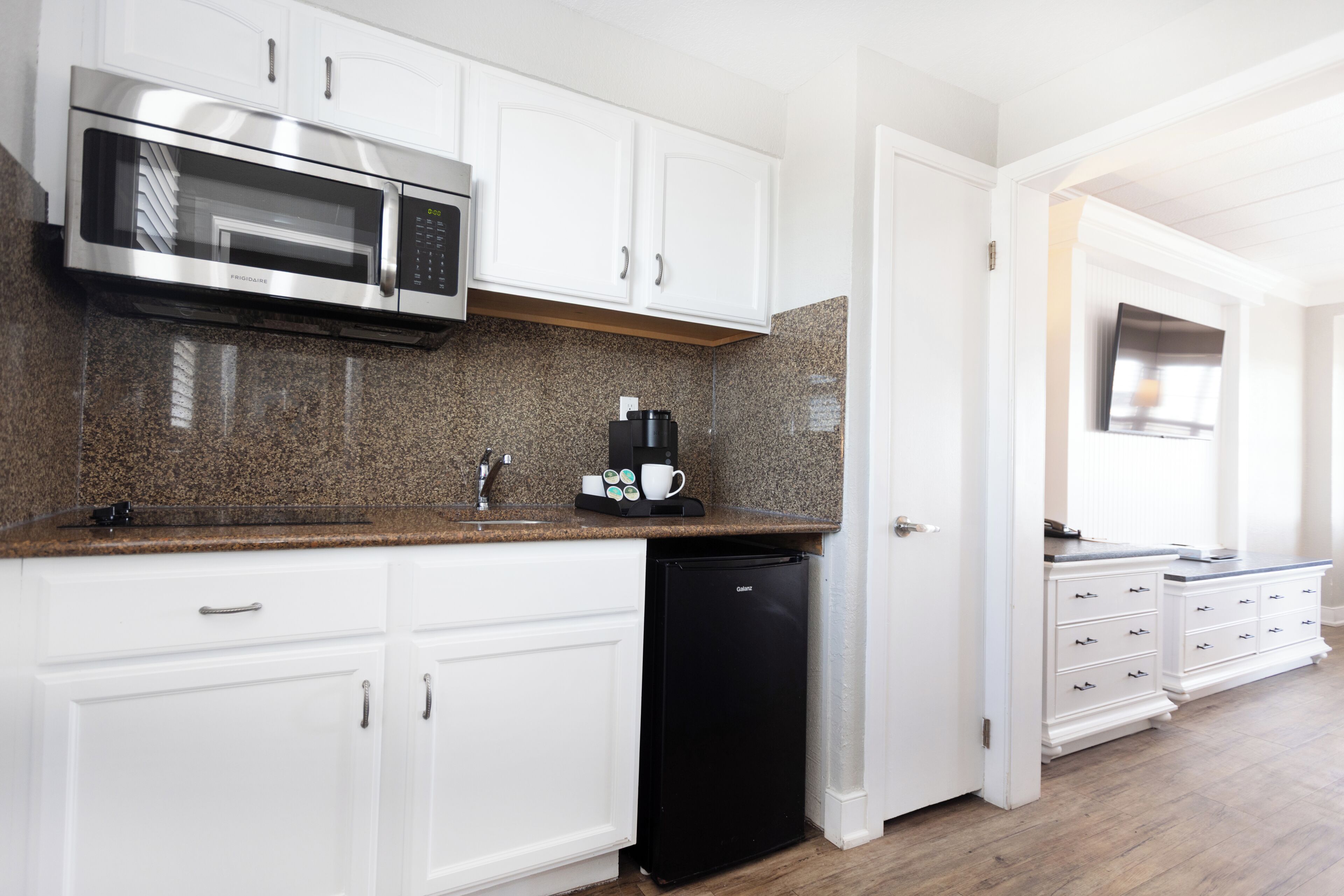 A kitchen with white cabinets, a stainless steel microwave, a coffee maker, and a black dishwasher.