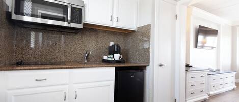 A kitchen with white cabinets, a stainless steel microwave, a coffee maker, and a black dishwasher.