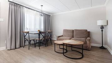 A room with a dining table, chairs, a sofa, a lamp, and a window with curtains.