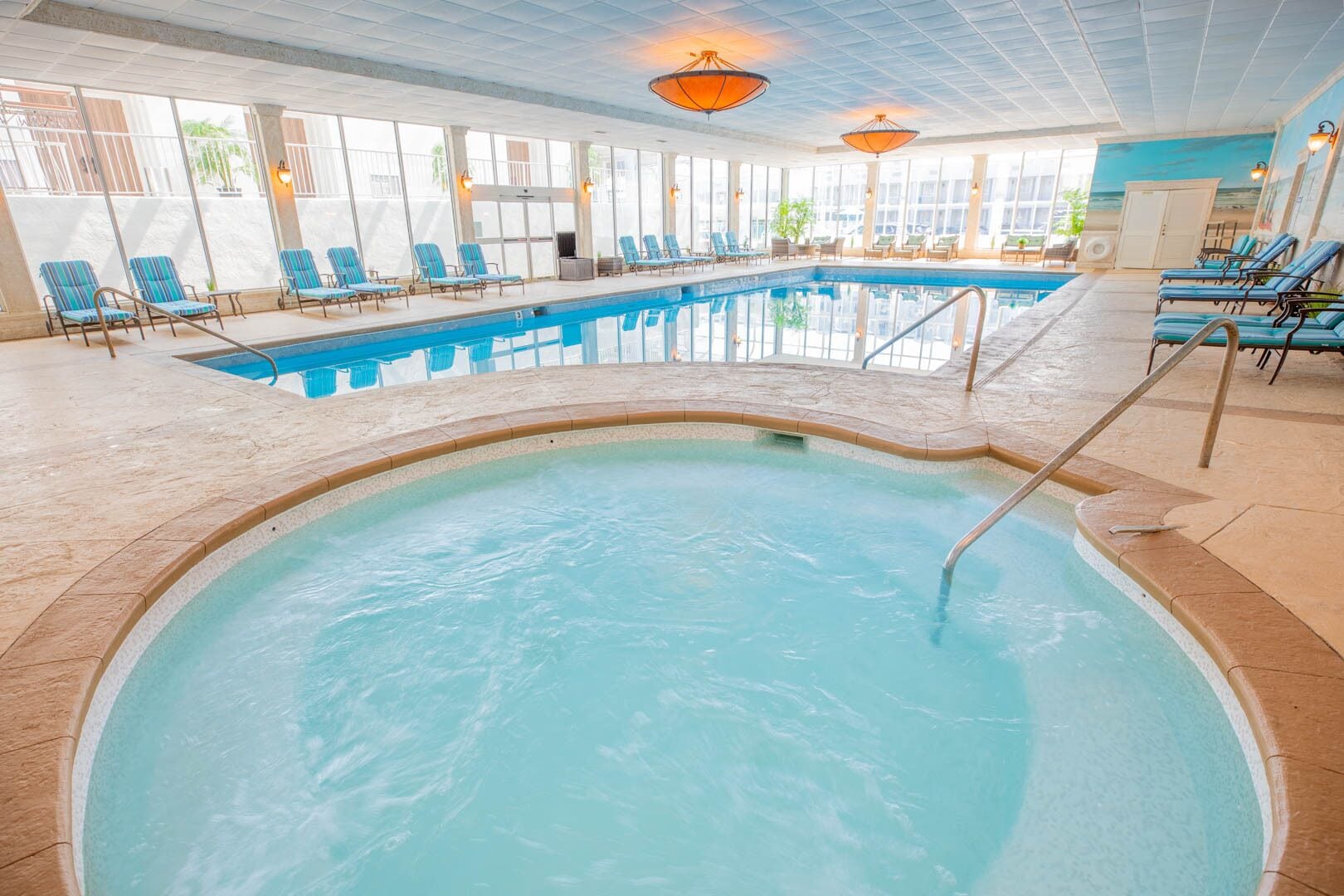 Una piscina interior con agua cristalina y azul, rodeada de sillas de descanso y suelo de baldosas.