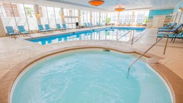 Una piscina interior con agua cristalina y azul, rodeada de sillas de descanso y suelo de baldosas.
