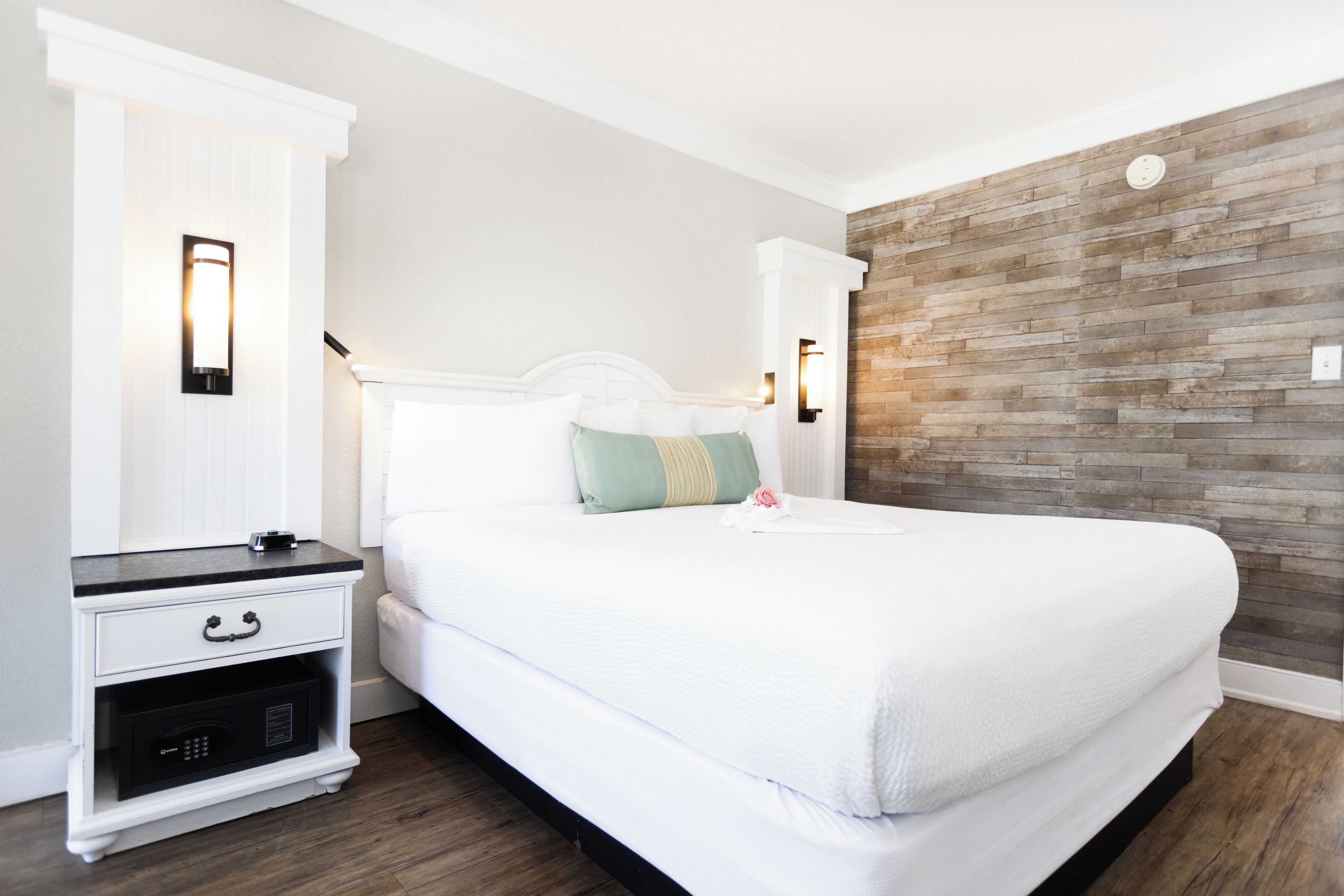 A neatly arranged bedroom with a bed, bedside table, and a wall-mounted light fixture.