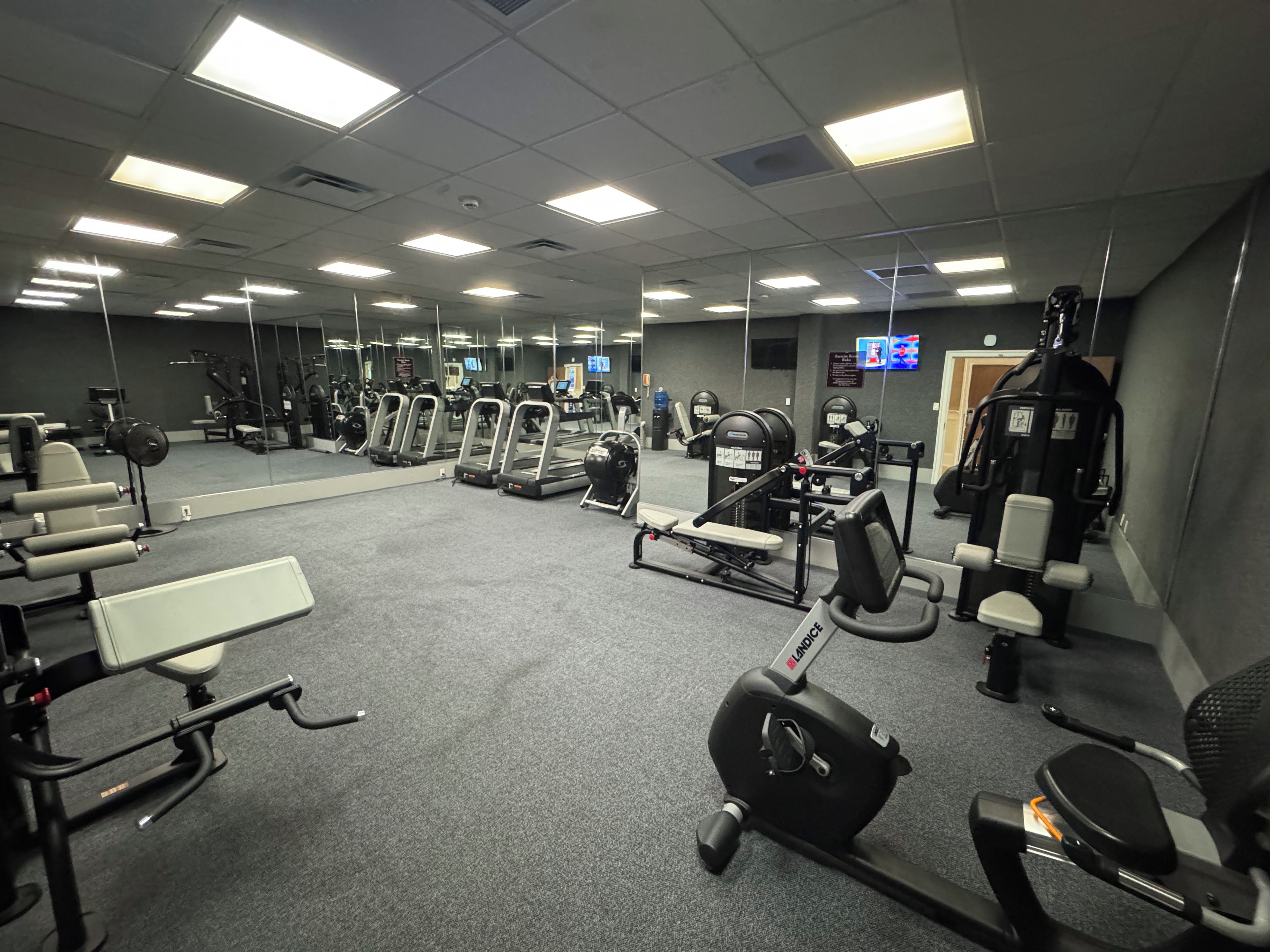 Une salle de sport équipée de divers appareils d’exercice, dotée d’un mur miroir et d’un éclairage au plafond.