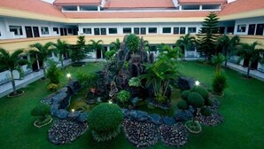 Un patio con una fuente central, rodeado de setos cuidados y palmeras.