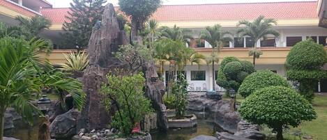 A courtyard with a rock formation, a small pond, and various tropical plants.