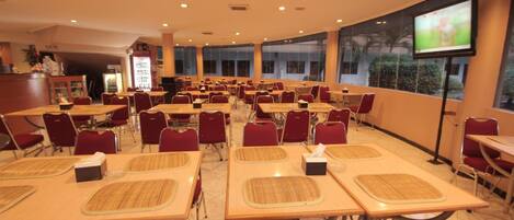 Un salón de conferencias con varias mesas y sillas, una pantalla de proyección y una máquina expendedora.