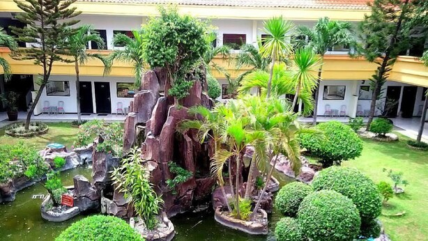 Un patio con un jardín de rocas, un pequeño estanque y diversas plantas tropicales.
