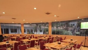 Una sala de conferències amb taules i cadires, una pantalla gran i finestres amb vista a zones verds.
