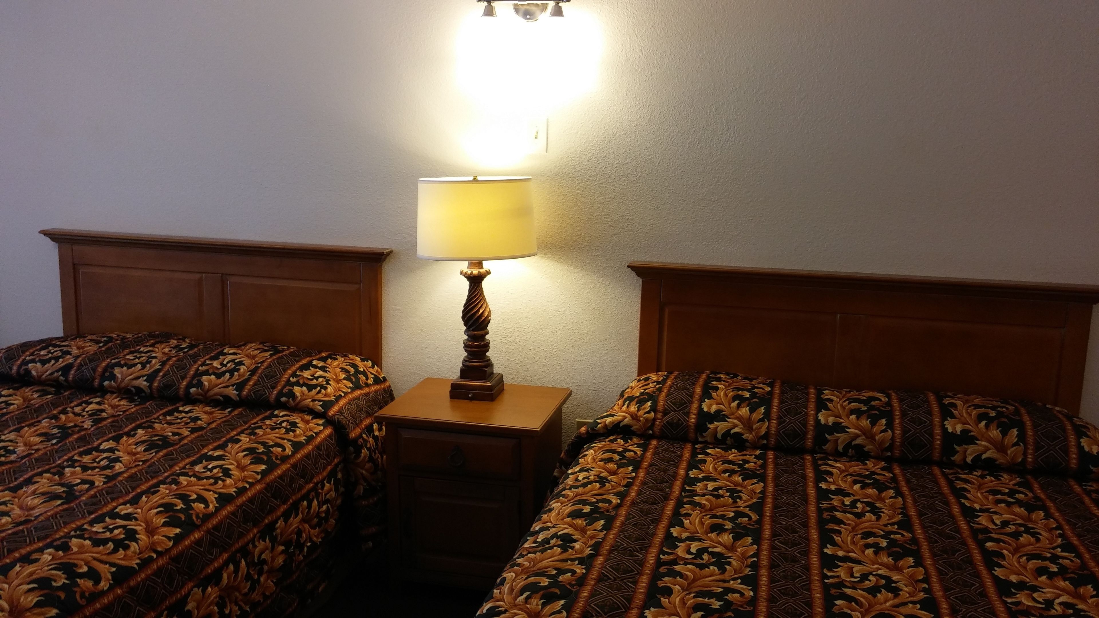 A hotel room with two single beds, a nightstand, and a lamp.