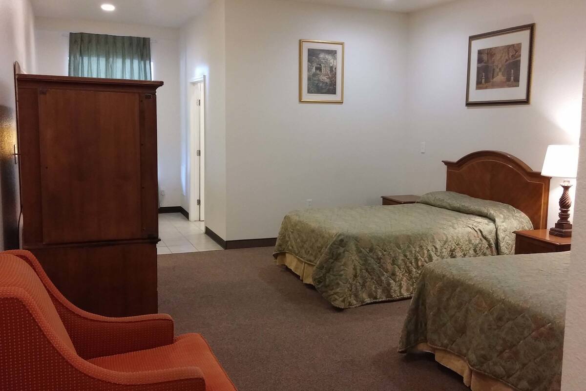 Hotellihuone, jossa on kaksi sänkyä, puinen vaatekaappi, työpöytä lampun kanssa ja kaksi kehystettyä kuvaa seinällä.