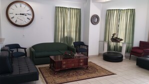 A living room with a green sofa, a wooden coffee table, a black ottoman, and a large wall clock. - Country Regency Inn & Suites (Manvel)