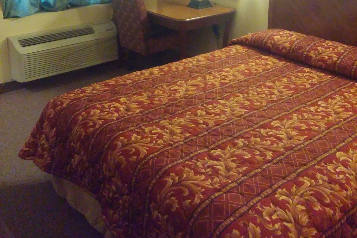 Hotellihuone, jossa on sänky, työpöytä, tuoli, lamppu ja ikkuna, jossa on verhot.
