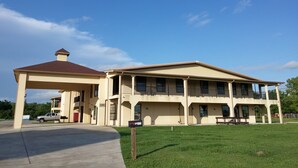 A two-story building with a covered outdoor area and a grassy lawn. - Country Regency Inn & Suites (Manvel)