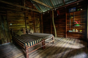 A rustic wooden room with a bed, shelves with decorative items, and a sloped ceiling. - Ella Eco Lodge (Ella)