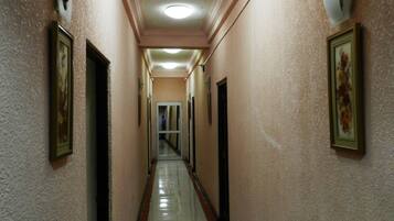 A long, narrow hallway with a tiled floor and cream-colored walls. There are doors on both sides, and the walls are decorated with framed pictures.