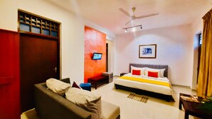 A hotel room with a bed, a sofa, a television, a ceiling fan, and a window with curtains. - Hotel Dorset (Negombo)