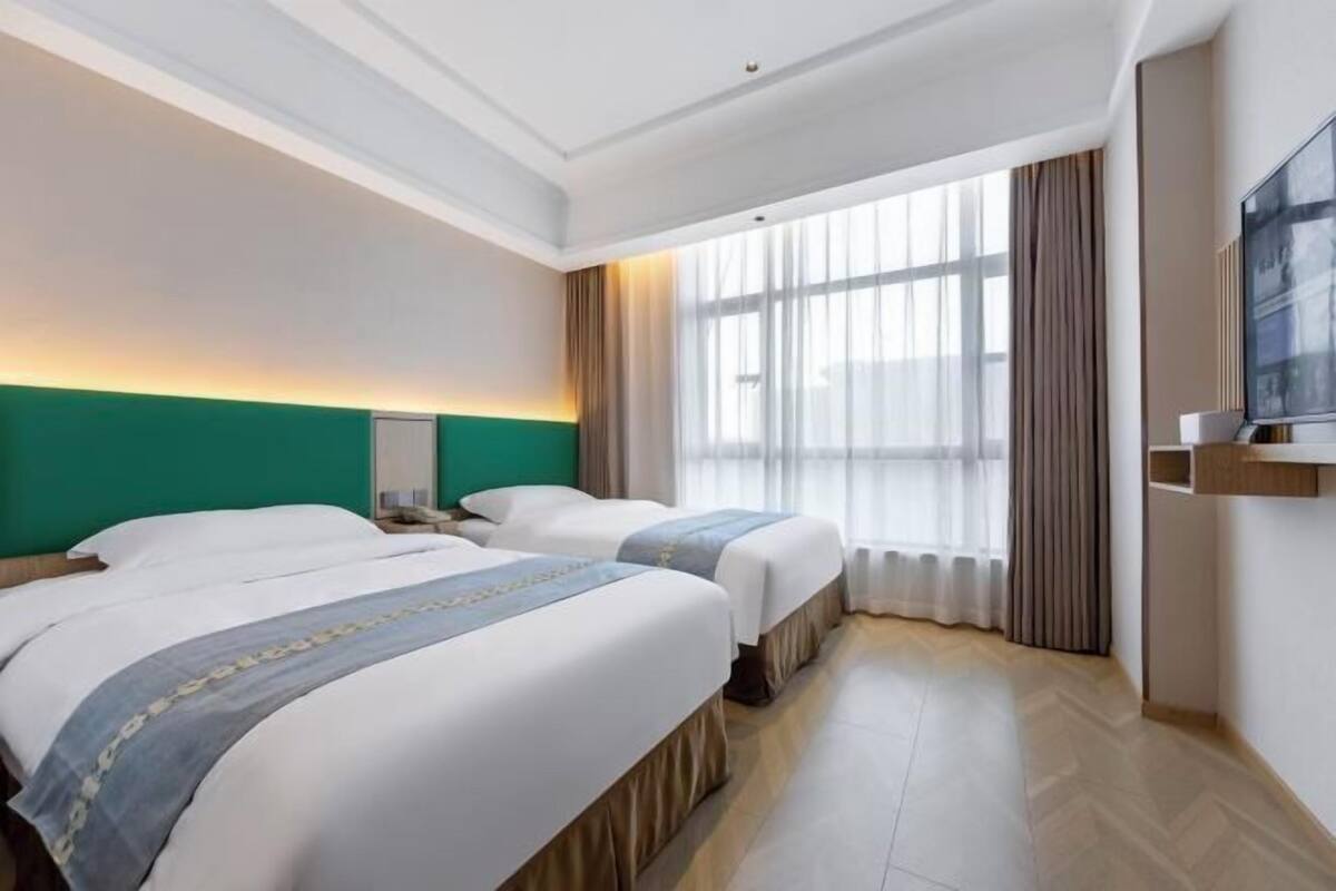 A hotel room with two beds, a large window with curtains, a flat-screen TV, and a wooden floor.