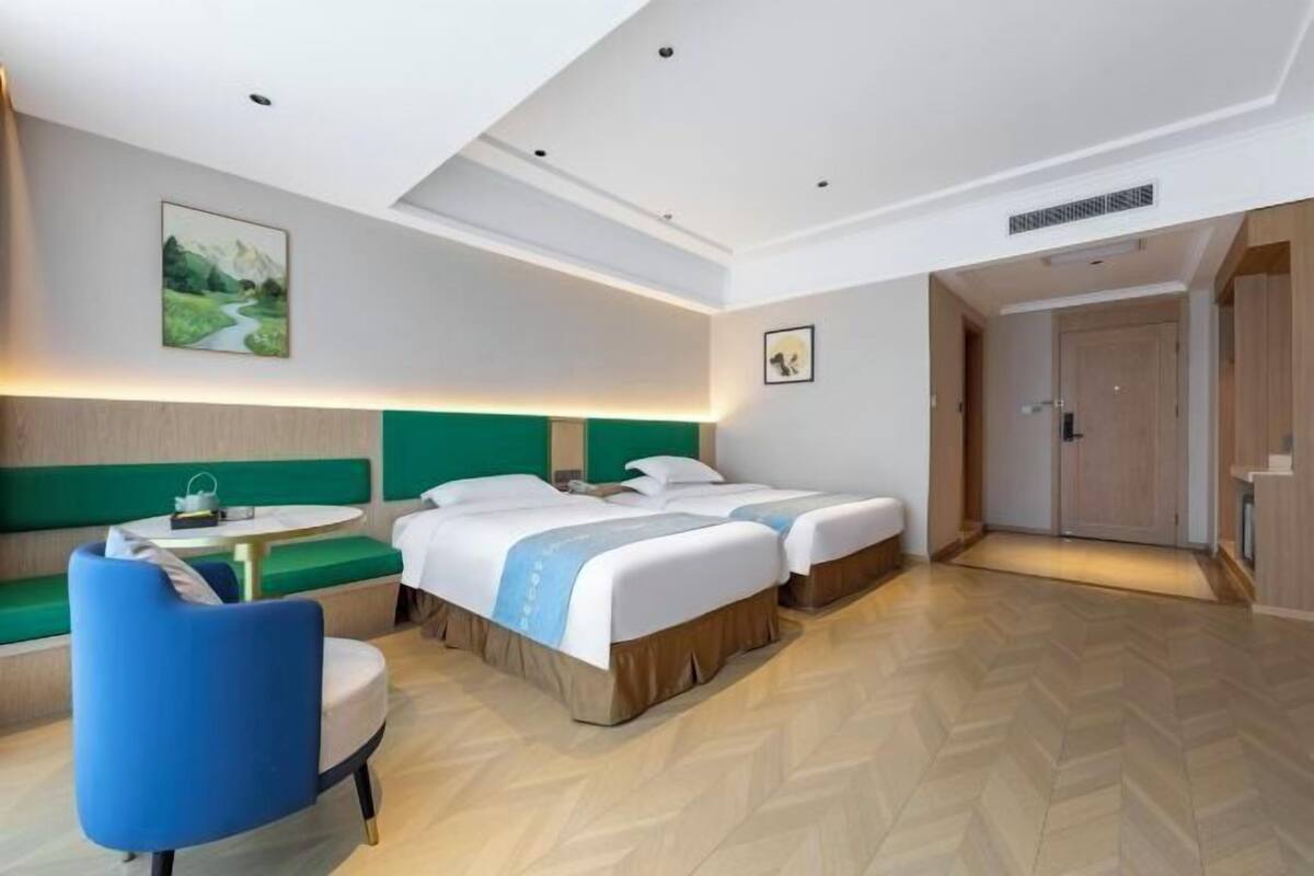 A hotel room with two beds, a round table, a blue chair, and a green sofa.