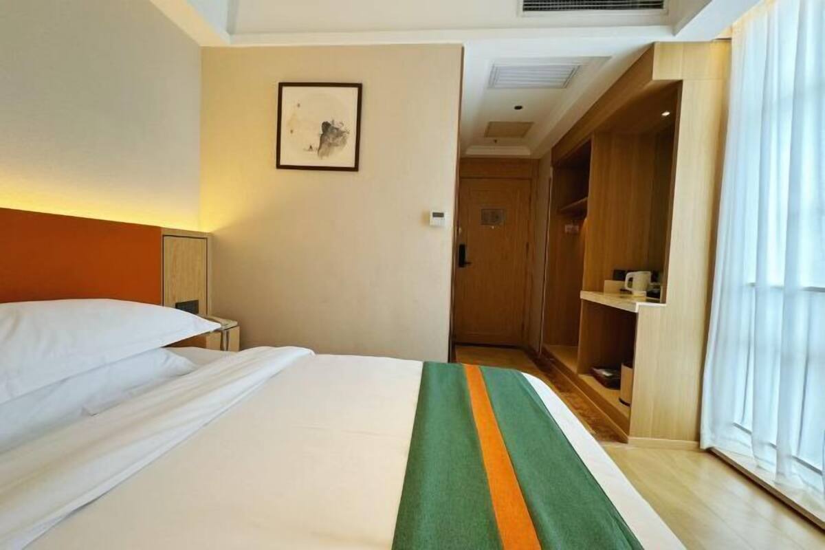 A hotel room with a bed, a bedside table, a framed picture on the wall, and a wooden wardrobe.