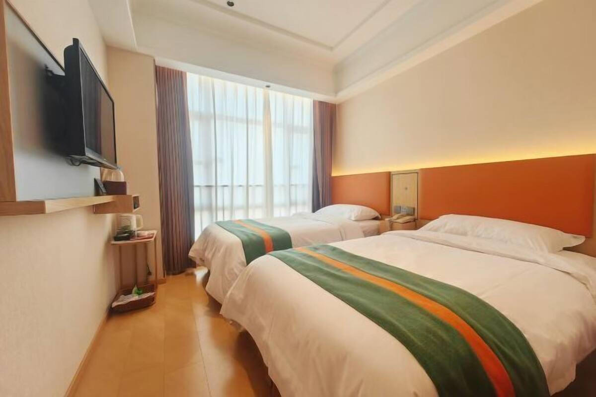 A hotel room with two beds, a TV, a bedside table, a nightstand, and a window with curtains.