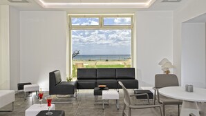 A modern room with a large window, a black sofa, a small table with drinks, and a round table with chairs.