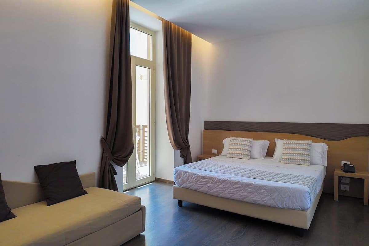 Una habitación de hotel con cama, sofá y mesita de noche.