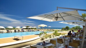 A poolside area with lounge chairs and umbrellas, a pool, and a view of the ocean.