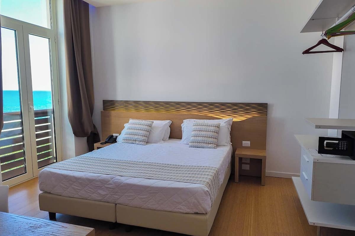 Habitación de hotel con cama, mesitas de noche, armario y vista al mar.
