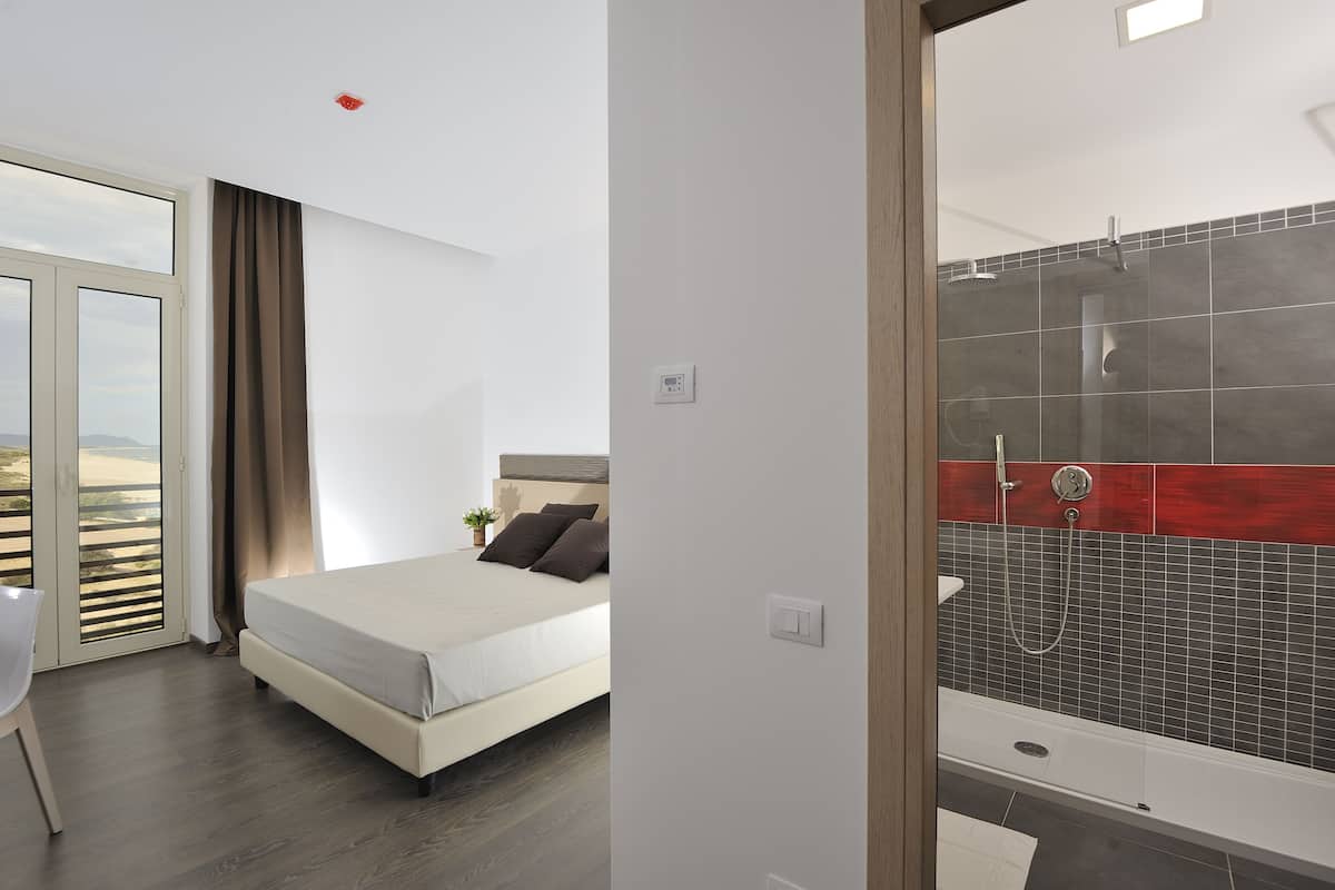 Un dormitorio con cama, una silla, un ventanal con cortinas y vistas al exterior.