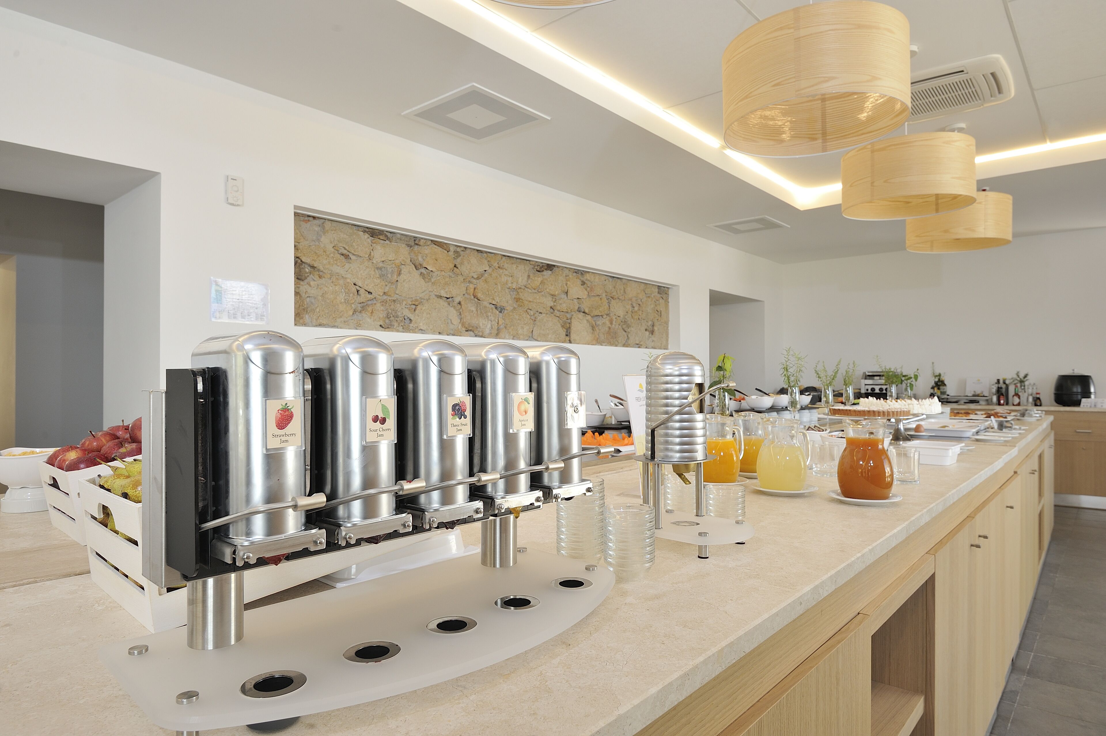 A modern kitchen with a juice dispenser, a stone backsplash, and wooden cabinets.