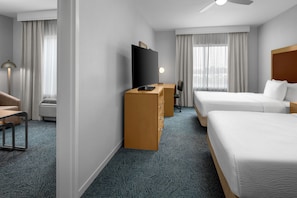 A hotel room with two beds, a desk with a chair, a TV, and a ceiling fan.