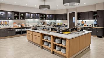 A modern kitchen with a central island, dark cabinets, and a variety of food dispensers.