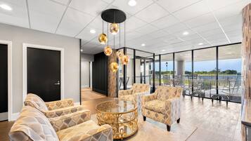 A modern interior with patterned furniture, a glass coffee table, pendant lighting, and a view through large windows.