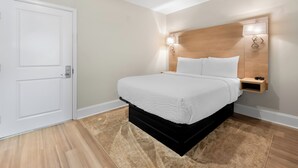 Un dormitorio con cama, mesita de noche, lámpara de pared y una puerta.