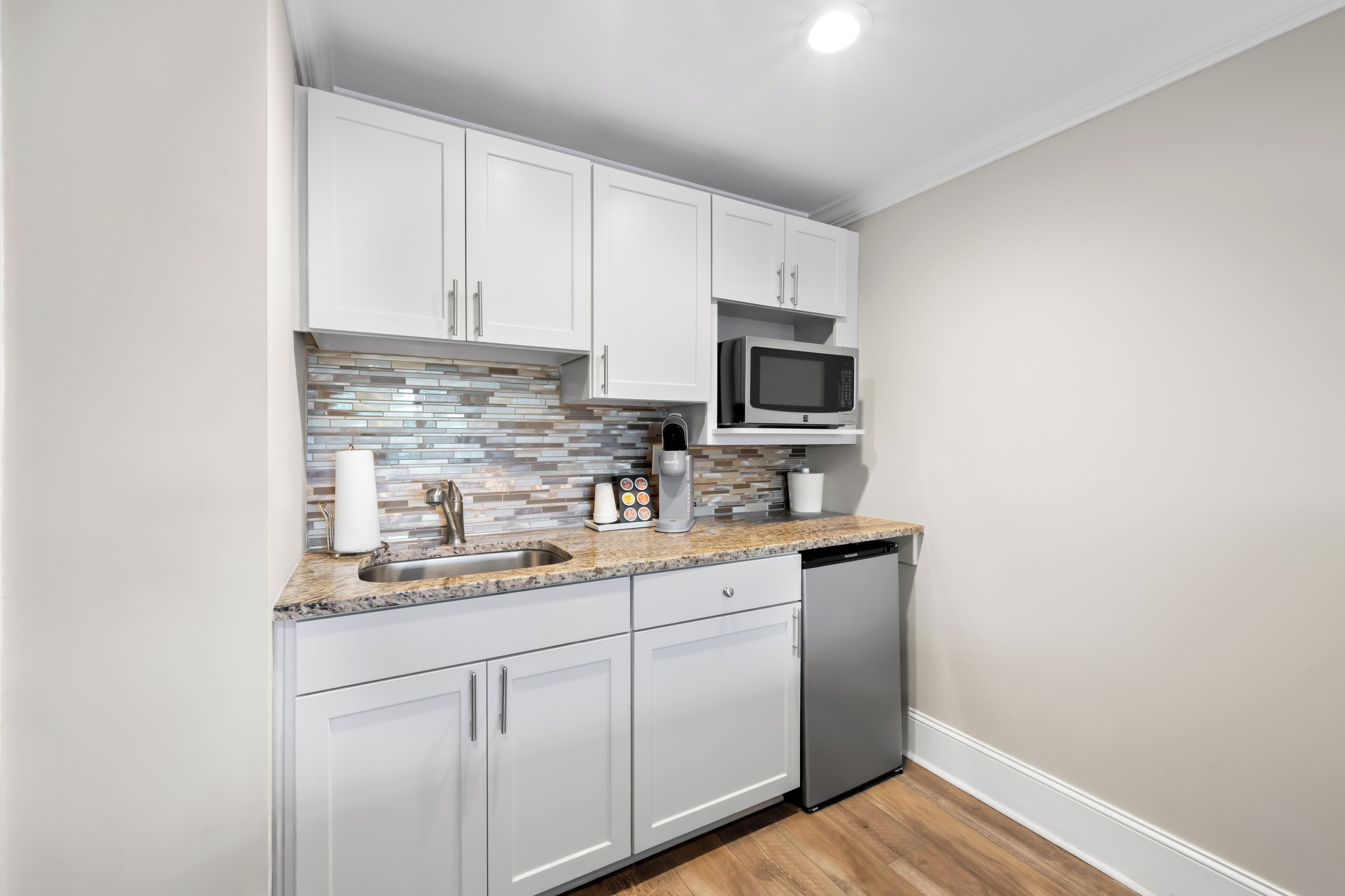 A compact kitchen with white cabinets, a microwave, a coffee maker, and a dishwasher.