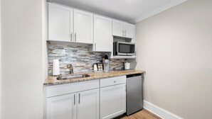 Cocina compacta con armarios blancos, microondas, cafetera y lavavajillas.