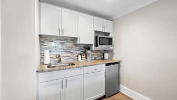 A compact kitchen with white cabinets, a microwave, a coffee maker, and a dishwasher.