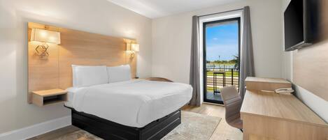 A hotel room with a bed, bedside tables, a desk, a chair, a TV, and a balcony with a view.