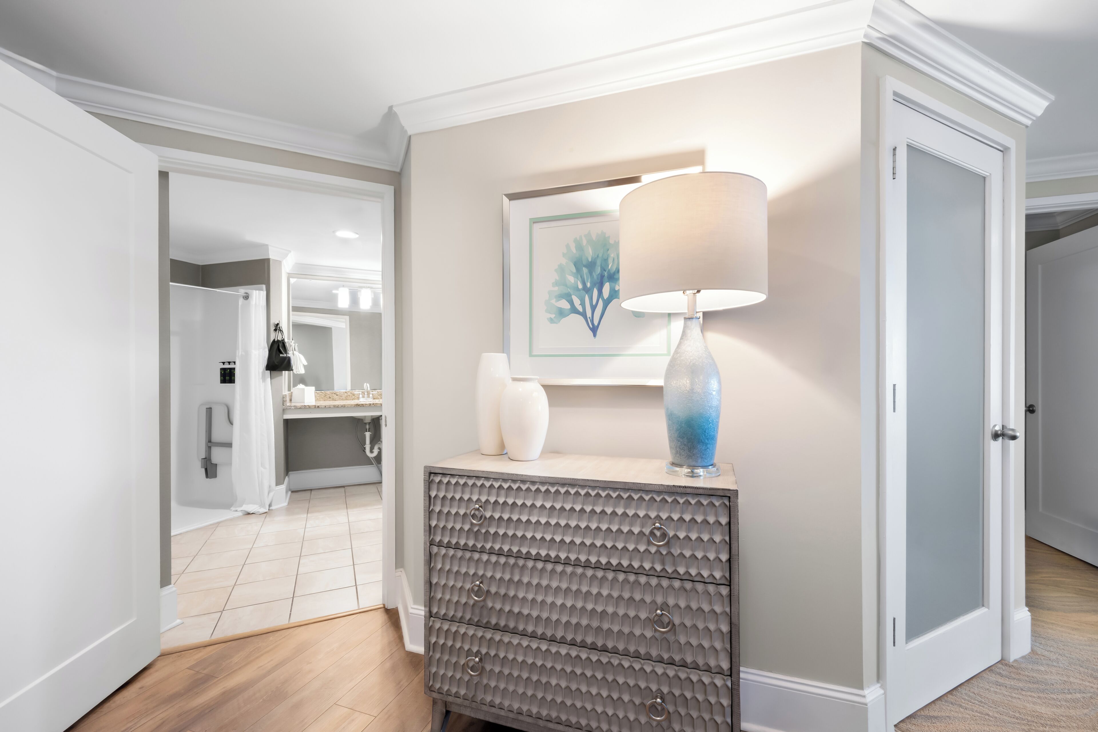 A hallway with a grey textured dresser, a white lamp, and a framed artwork on the wall.