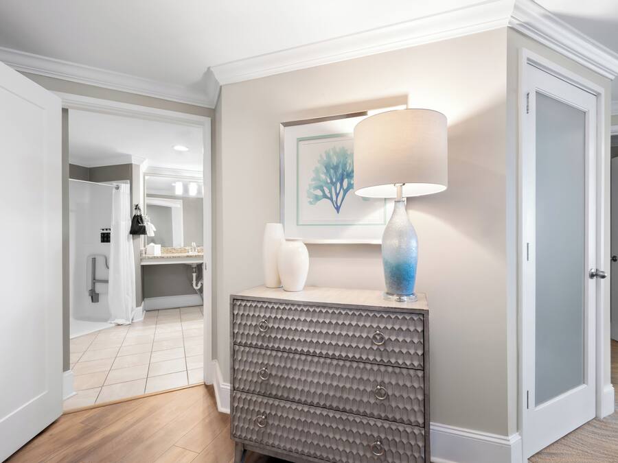 A hallway with a grey textured dresser, a white lamp, and a framed artwork on the wall.