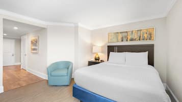 A hotel room with a large bed, a chair, a nightstand with a lamp, and a painting on the wall.