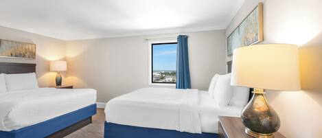 A hotel room with two beds, a window with a view, a lamp, and a painting on the wall.